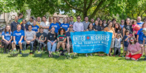 UN35 members arranged in two rows, with potted plants in the foreground and a large tree in the background.